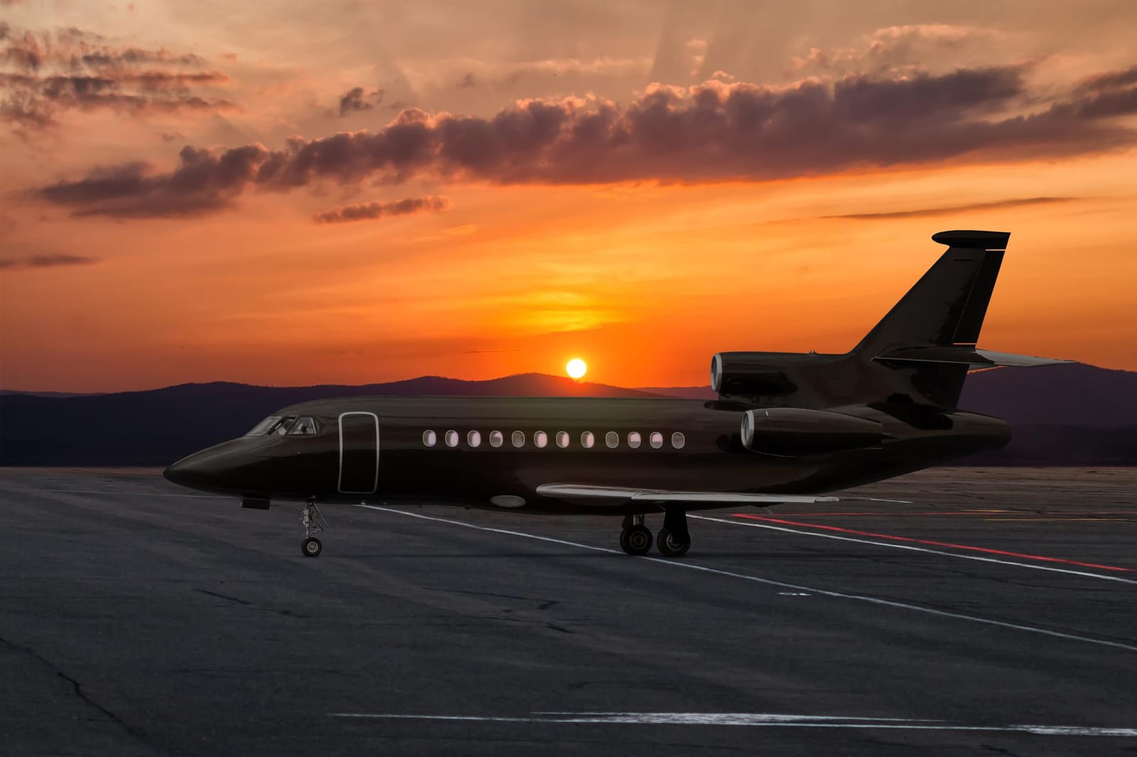 Silhueta de um jato executivo no pátio do aeroporto contra um pôr do sol alaranjado.